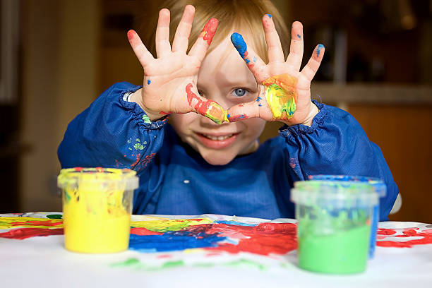Toddler boy holds up his colorful and messy hands covered with fingerpaint. france.